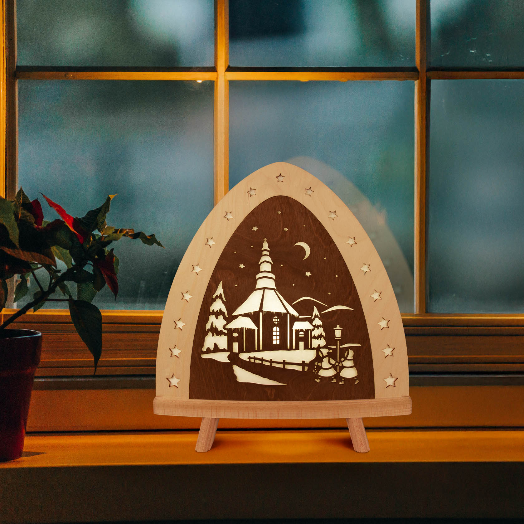 LED Standleuchte mit der Silhouette der Seiffener Kirche, umgeben von Tannenbäumen und einem Mond. Die Leuchte steht vor einem Fenster.
