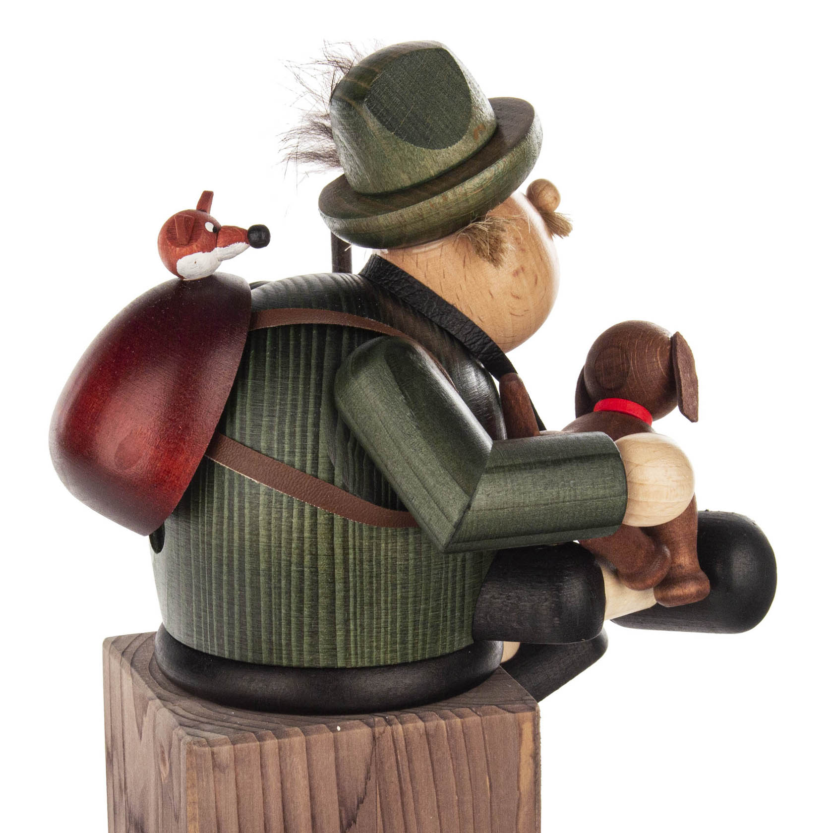 Holzfigur: Ein Förster mit grüner Jacke und Hut sitzt als Kantenhocker. Ein Hund auf dem Schoß und ein roter Rucksack mit kleinem Tier darauf.