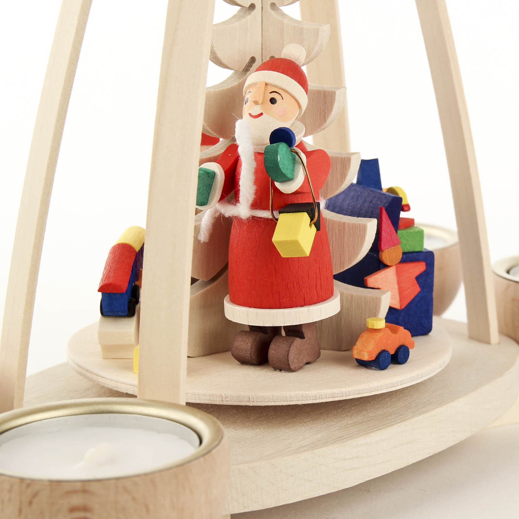 Holzpyramide mit Weihnachtsmannfigur in der Mitte, umgeben von farbigem Spielzeug und Teelichthaltern.