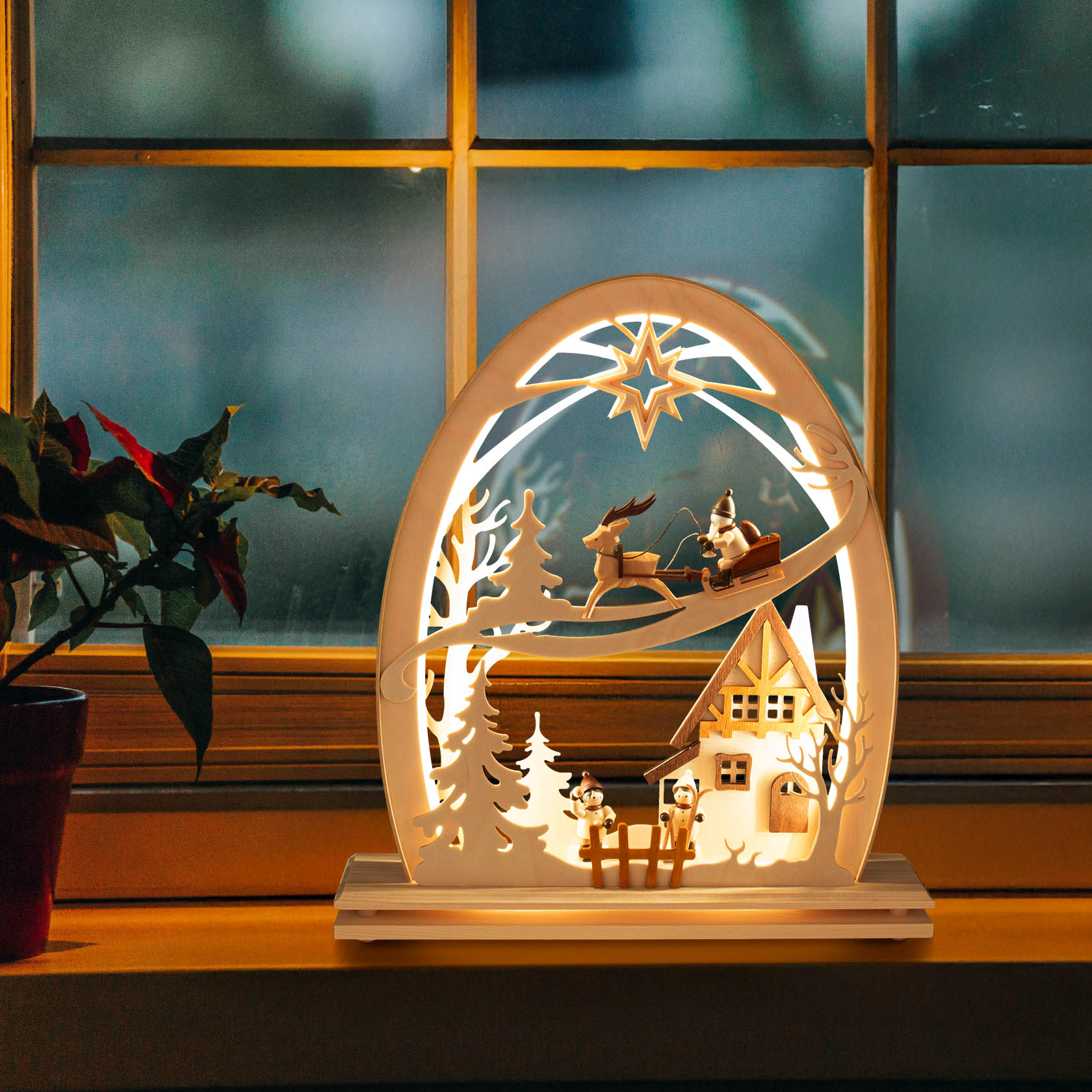 Ein elektrischer Erzgebirgsbogen mit LED-Beleuchtung zeigt einen Nikolaus auf einem Schlitten, gezogen von einem Rentier, über einem winterlichen Dorf.