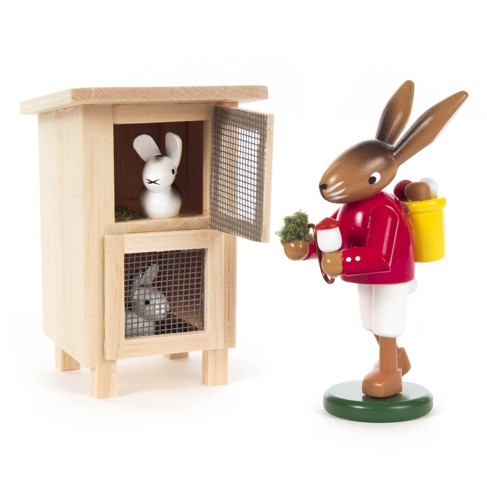 Holzfigur eines Hasen in roter Jacke und weißer Hose mit gelbem Korb auf dem Rücken, der vor einem Hasenstall mit zwei Hasen steht.