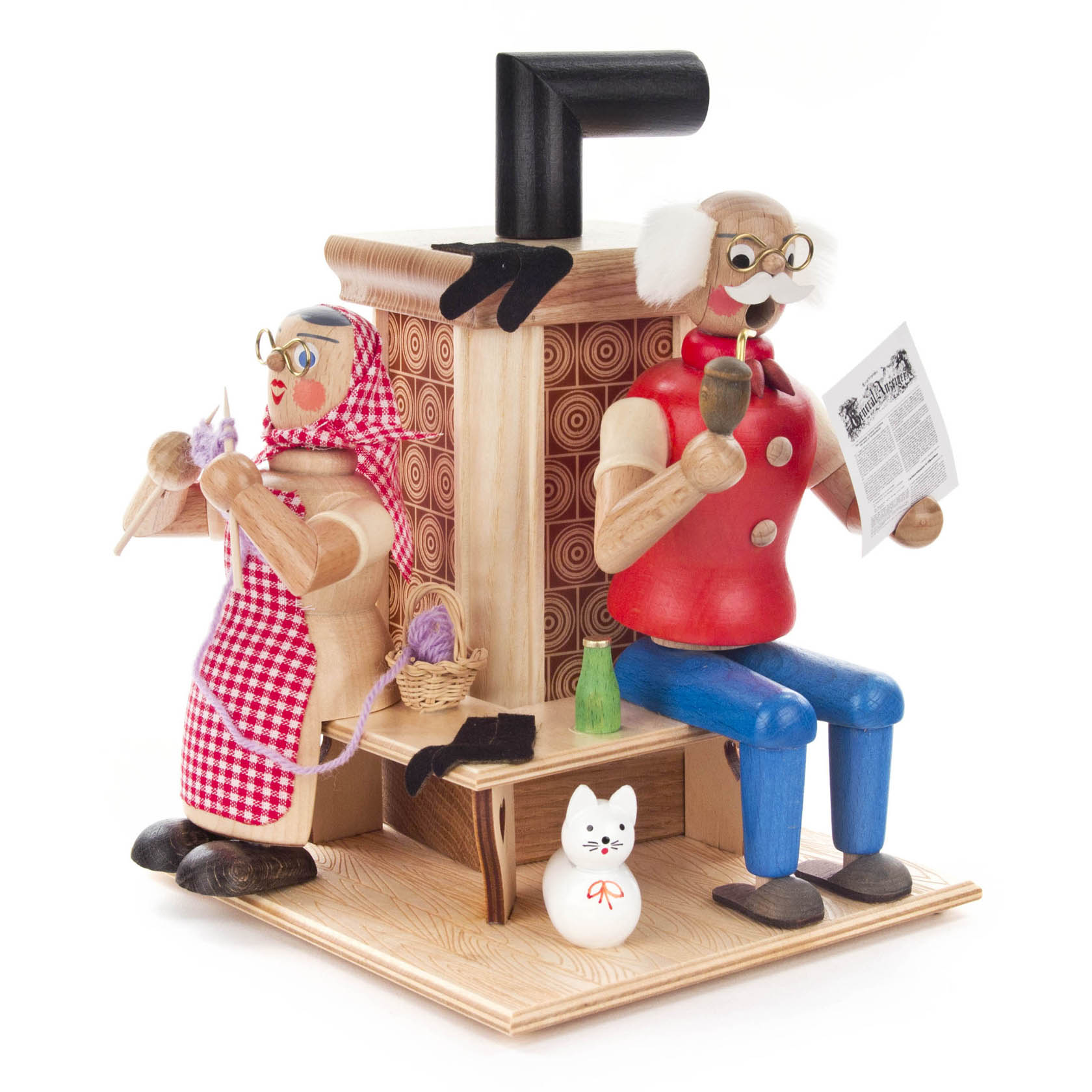 Holzfiguren eines älteren Mannes mit Zeitung und einer Frau mit Strickarbeit, beide sitzen nebeneinander an einem Holzofen, Katze zu ihren Füßen. im Dregeno Online Shop günstig kaufen