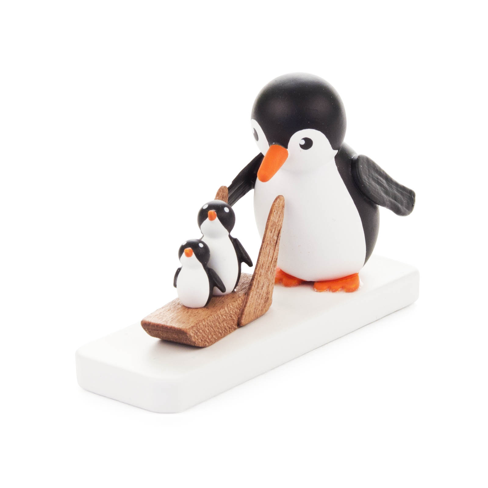 Ein großer Pinguin schiebt zwei kleine Pinguine auf einem Holzschlitten. Die Pinguine stehen auf einer weißen Basis. im Dregeno Online Shop günstig kaufen