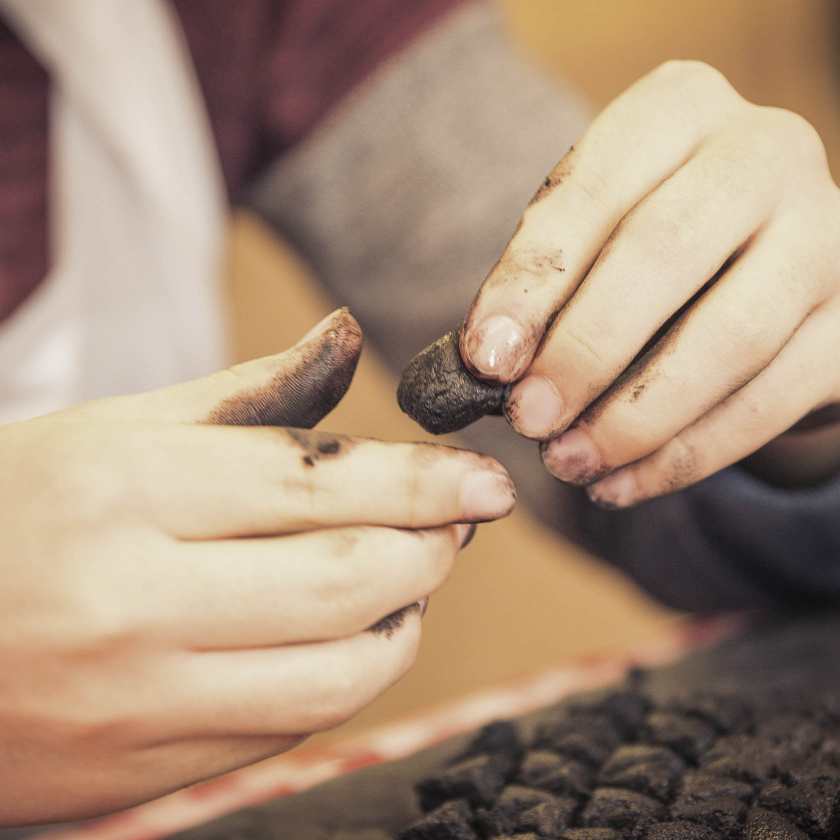 Nahaufnahme von zwei Händen, die ein kleines, schwarzes Räucherkerzchen formen. Die Finger sind von dem Material der Räucherkerze geschwärzt.