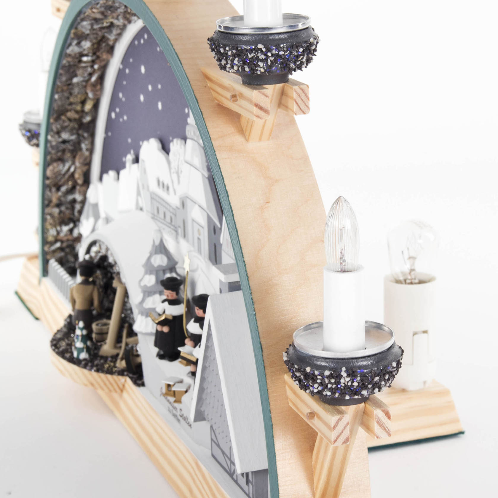 Ein beleuchteter Schwibbogen zeigt ein Seiffener Dorf mit Kurrende-Sängern und einem Bergwerk, dekoriert mit glitzernden Details und elektrischen Kerzen.