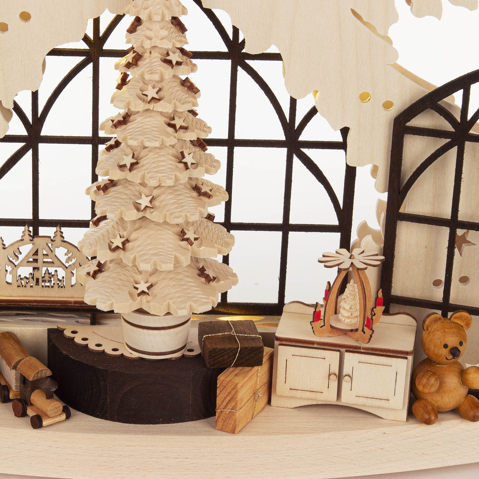 Ein Schwibbogen zeigt eine Weihnachtsstube mit einem Tannenbaum, einem Bär, einer Kerze, Holzklötzen, und einem beleuchteten Fenster im Hintergrund.