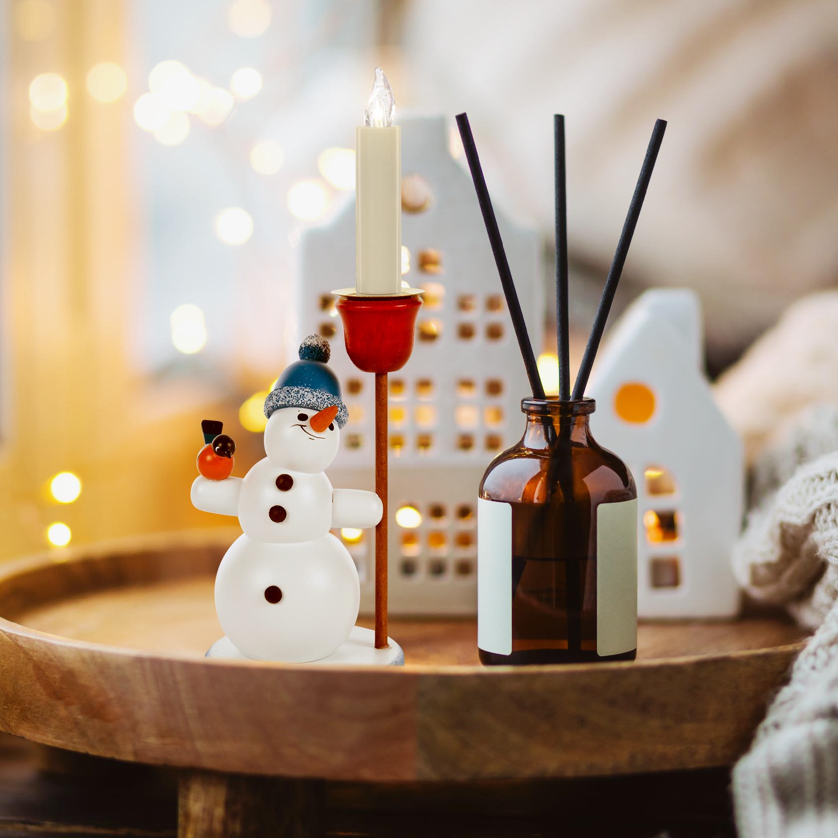 Ein Schneemannfigur mit blauer Pudelmütze hält einen roten Kerzenhalter für eine dünne Kerze. Er steht auf einem Tablett neben einer braunen Flasche.